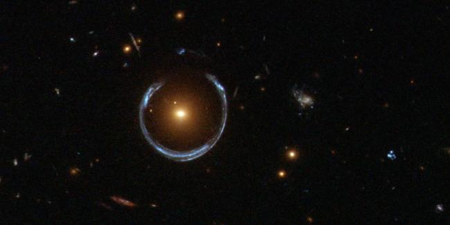 Obraz odległej niebieskiej galaktyki zniekształcony przez efekt soczewkowania grawitacyjnego bliższej galaktyki czerwonej.